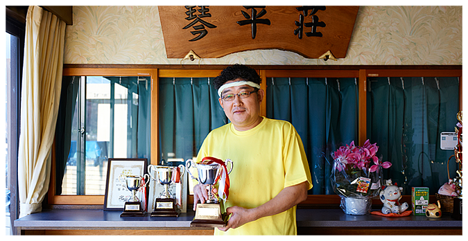 こちらが店主・掛神 淳氏。お取り寄せラーメンオブザイヤーのトロフィーを 手渡してきました。パンチパーマが特徴。 